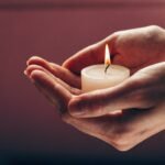 Mãos protegendo a chama suave de uma vela